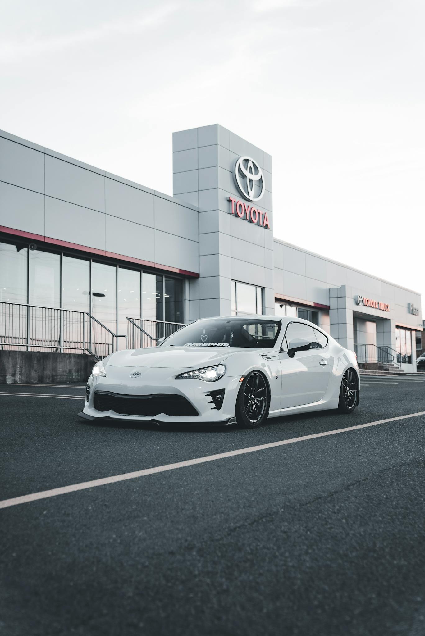 Stylish modern white car parked in front of a Toyota dealership showroom.